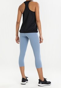 Top nero senza maniche con design racerback, abbinato a leggins capri blu chiaro. L'outfit presenta un look sportivo e sneakers nere texturizzate.