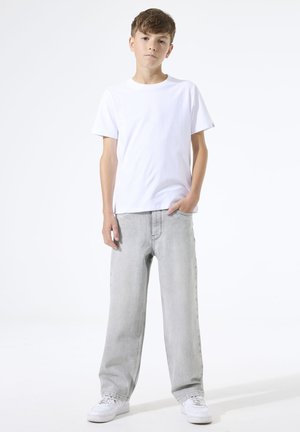 Boy standing, wearing a plain white t-shirt, light gray wide-leg jeans, and white sneakers, against a white background.