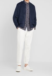 Námořnická sametová bomber bunda přes námořnickou květinovou košili s knoflíky, spárovaná s bílými kalhotami a bílými teniskami. Hladké textury a volný střih.