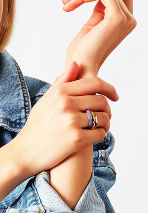 Mains ajustant un poignet avec deux bagues à un doigt, une en or et une lavande, portant une manche de veste en denim bleu clair.