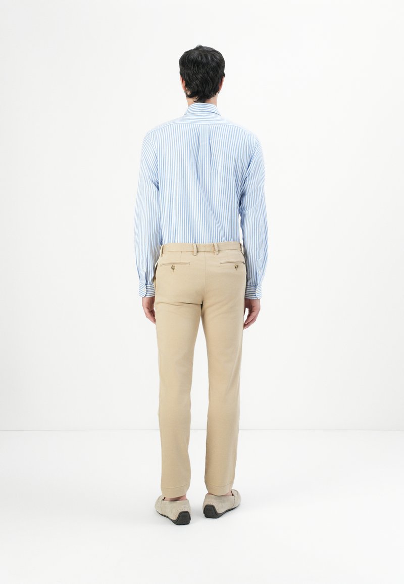 Jasnoniebieska i biała, w paski, koszula z długim rękawem w połączeniu z beżowymi spodniami, z tylnymi kieszeniami i dopasowanym krojem. Gładkie białe tło.