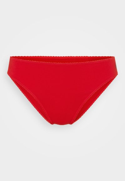 Piros bikini alsó, amely sima anyagból készült, alacsony derekú kialakítással, fodros szélekkel a derékrészen, és minimalista stílussal, további minták nélkül.