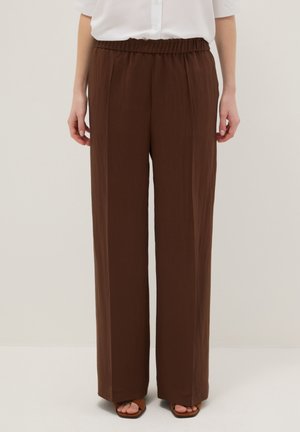 Pantalon marron droit avec taille élastique, porté avec une chemise blanche rentrée et des sandales marron à bouts ouverts.