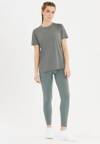 Grau kurzärmliges Sport-T-Shirt kombiniert mit passenden Leggings, die eine glatte Textur, einen figurbetonten Schnitt und weiße Sneaker aufweisen.
