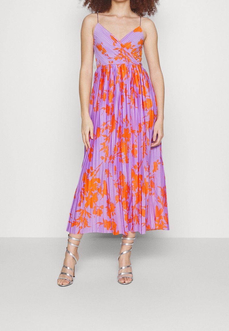 Robe longue violet clair avec un motif floral orange, dotée d'une jupe plissée, d'un décolleté en V et de fines bretelles. Associée à des talons argentés à brides.