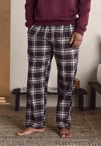 Rutig pyjamasbyxor i mörkpurpur, vitt och grönt. Har ett elastiskt midjeband och sidofickor, tillverkade av mjukt tyg med en avslappnad passform.