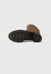 Bruine suede enkellaars met een getextureerde bovenkant, rubberen zool met een profielpatroon en een zijrits voor gemakkelijk aan- en uittrekken.