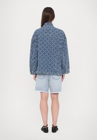 Dżinsowa kurtka z powtarzającym się wzorem diamentów, o luźnym kroju, jasnoniebieskiego koloru i kołnierzu. Noszona z jasnoniebieskimi szortami dżinsowymi i czarnymi butami.