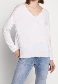 Weißer, leichter Pullover mit langen Ärmeln, V-Ausschnitt, lässiger Passform und geripptem Saum. Der Stoff wirkt leicht transparenter mit einer glatten Textur.