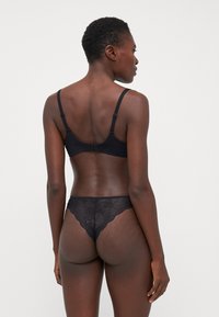 Schwarzes Spitzen-Bra und String-Set mit floralen Mustern, verstellbaren Trägern und Haken- und Ösenverschluss. Die transparente Textur steht im Kontrast zu den soliden Bereichen.