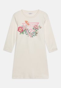 Kermanvärinen pitkähiha mekko, jossa kukkakuvio ja vaaleanpunainen kolmionmuotoinen logo, jossa teksti "GUESS U.S.A.", keskellä edessä.