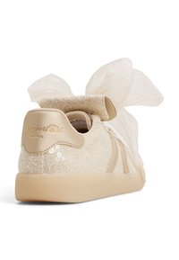 Beżowe sneakersy pokryte koronką z satynowymi akcentami, z dużą przezroczystą kokardą na kołnierzu i teksturowanym, cekinowym wzorem na pięcie.