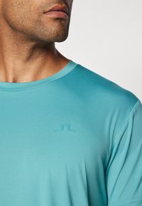 Turkise sports t-shirt lavet af letvægtsstof, med rund hals og diskret præget logo på brystet.