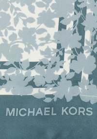Motif floral bleu clair sur un fond blanc, présentant de grandes fleurs avec des accents verts. Le texte "MICHAEL KORS" est en bas.