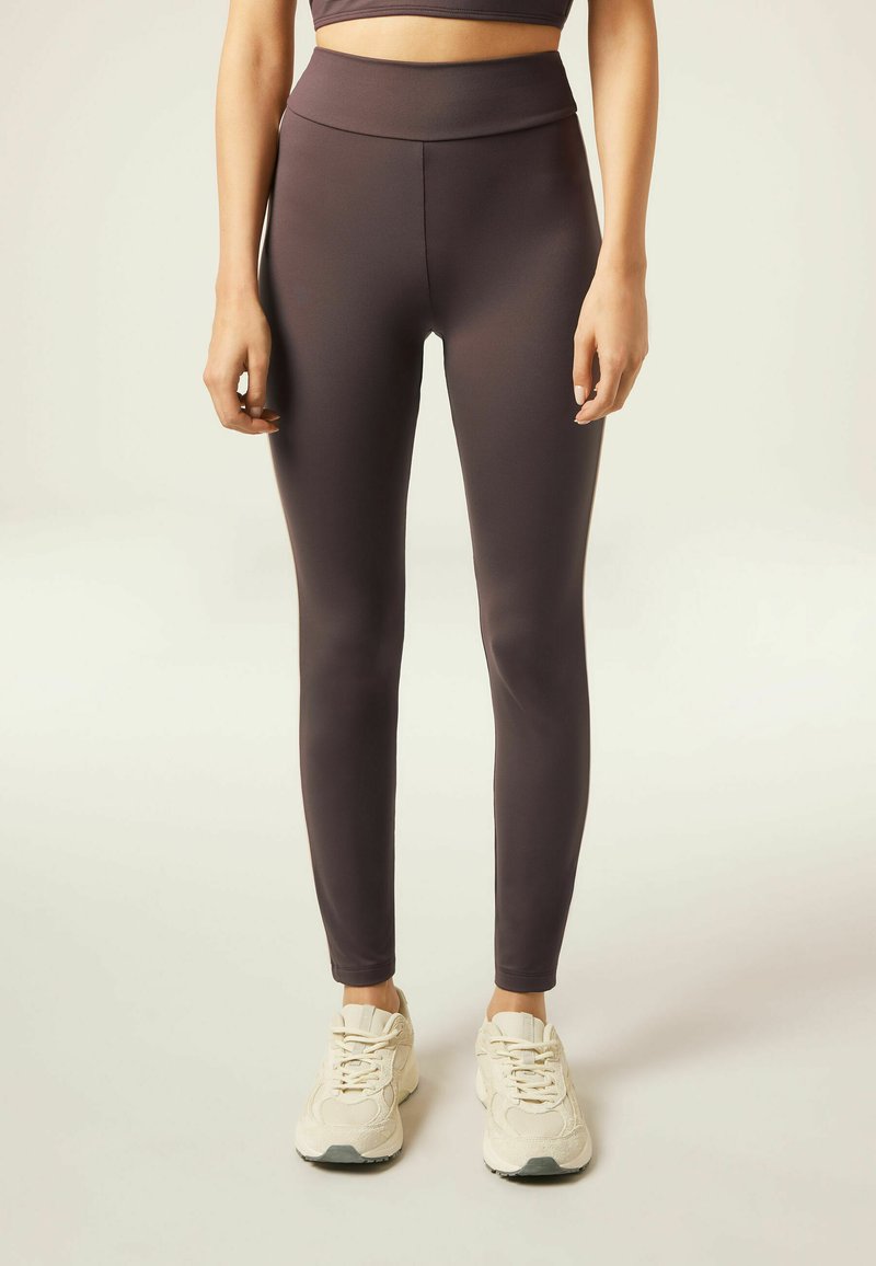 High-waisted, slim-fit leggings in dark brown stretchy material, paired with light-colored athletic shoes. Smooth texture, no visible patterns.