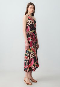 Maxikleid mit bunten Blattmustern auf einem leichten Stoff, mit einem taillierten Oberteil, tiefem Ausschnitt und dünnen Trägern.