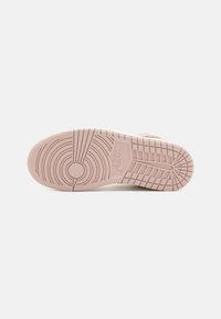 Sole butów Nike w jasnoróżowym kolorze, z teksturowaną powierzchnią z okrągłymi i liniowymi wzorami oraz wystającym logo z boku.