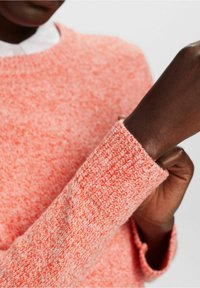 Neulottu neulepusero kirkkaassa korallin sävyssä, jossa on teksturoitu kuvio ja joustinneulotut hihansuut. Kangas näyttää pehmeältä ja muhkealta.