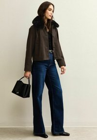 Bruine geruite cropped jas met een faux fur kraag, gecombineerd met donkerblauwe wijde jeans en een kleine zwarte handtas.