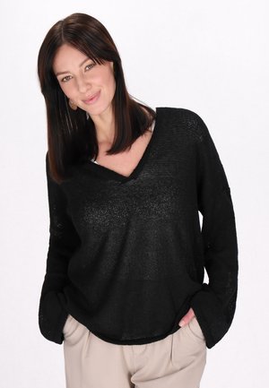 Pull en maille légère noir avec un décolleté en V profond et des manches longues. Présente une coupe ample et un tissu texturé. Associé à un pantalon beige.