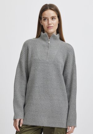 Pull en tricot gris avec un col montant et une fermeture éclair quart. Présente une texture côtelée, une coupe décontractée et des manches longues. Design à ourlet évasé.