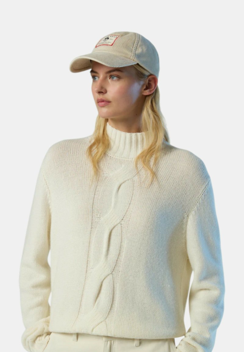 Maglione bianco lavorato a maglia con collo alto e motivo a treccia. Abbinato a un cappellino beige con patch logo. Texture morbida, vestibilità comoda.