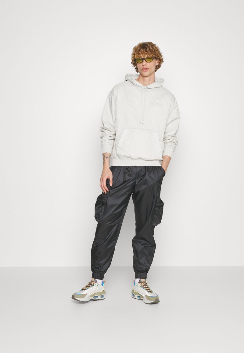 Hellgrauer Hoodie mit strukturiertem Muster, schwarze Cargohose mit elastischen Bündchen und mehrfarbige Sneaker mit massiven Sohlen.
