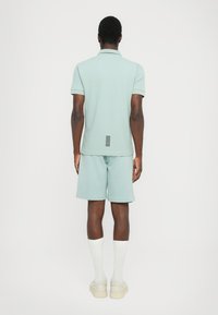 Camisa polo verde clara combinada com calções a condizer. Tecido texturizado com elementos de design nas costas e riscas em contraste. Meias brancas e ténis.