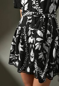 Robe noire et blanche à boutons, présentant des motifs floraux et de poissons, en tissu texturé, avec une taille cintrée et une jupe évasée ornée d'accents en œillets.