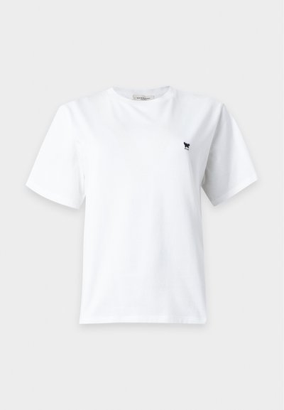 T-shirt blanc uni à manches courtes et col rond avec petit logo papillon noir sur le côté gauche de la poitrine sur fond gris clair.