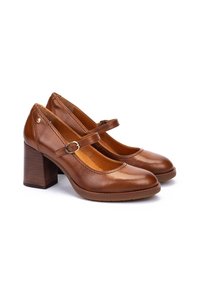 Talons Mary Jane en cuir brun avec un bout arrondi, une lanière avec une boucle en métal, et un talon en bois épais. Texture lisse.