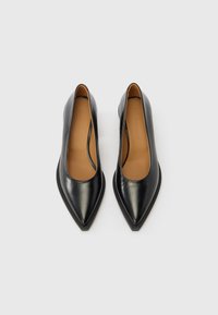 Μαύρα δερμάτινα παπούτσια με μυτερή μύτη και ταμπά εσωτερική σόλα, σε εμφάνιση από ψηλά πάνω σε φωτεινό γκρι φόντο.