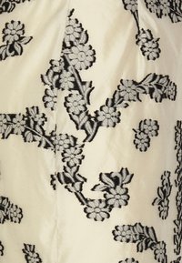 Brodert stoff i kremfarge med svarte blomster- og bladmotiver. Myk tekstur, detaljert stitching, og et fremtredende blomsterdesign gjennom hele.
