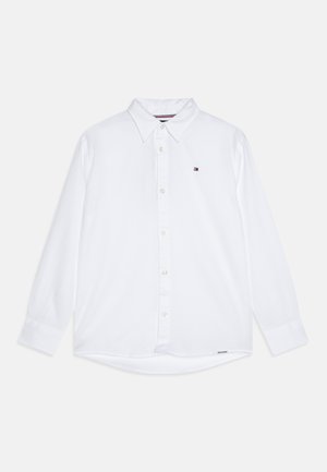 Camicia bianca a maniche lunghe con colletto a bottoni, dotata di un piccolo logo sul petto e orlo curvo. Il tessuto è texturizzato.