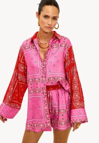 Roze en rode set met bandana-patroon, bestaande uit een shirt met lange mouwen en een broek, met een kraag en een textuurstof met paisley-ontwerpen.