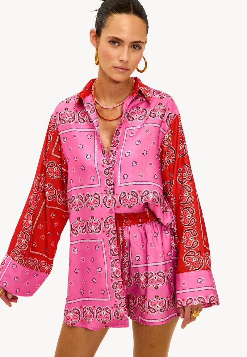 Roze en rode set met bandana-patroon, bestaande uit een shirt met lange mouwen en een broek, met een kraag en een textuurstof met paisley-ontwerpen.