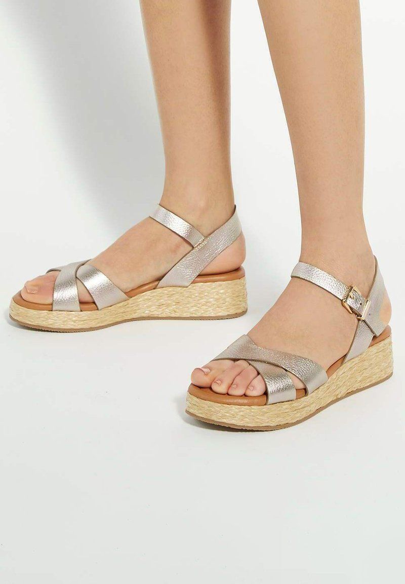 Metallic silver wedge sandals with cross straps, textured leather finish, jute-wrapped platform, and ankle buckle for secure fit.
