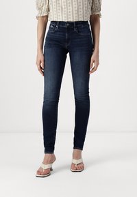 Mörkblå skinny jeans gjorda av denim. Har hög midja, slim fit och minimalistisk hårdvara. Matchas med ljusa sandaler.