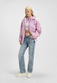 Lila kort jacka med fluffig textur, dragkedja och fickor. Kombinerad med ljusblå slitna jeans och vita platåsneakers.