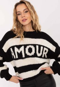 Schwarz-creme gestreifter Pullover mit grob gestrickter Textur, der prominent das Wort "AMOUR" in der Mitte zeigt. Lockerer Schnitt mit weiten Ärmeln.