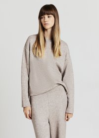 Hellbeiger Pullover mit langen Ärmeln und legerer Passform, aus einem weichen, strukturierten Stoff. Kombiniert mit passenden beigen Hosen.