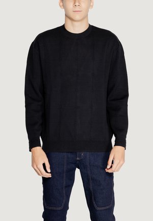 Pull en maille noire avec un motif texturé, col rond et manches longues, associé à un jean en denim bleu foncé.