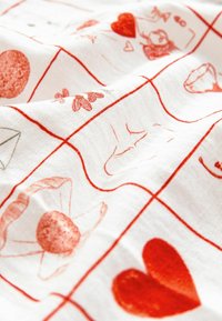 Biely materiál s červenými nákresmi zobrazujúcimi rôzne tvary, vrátane srdiečok, kvetov a geometrických tvarov, usporiadanými v mriežkovom vzore.