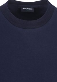 Marineblauwe katoenen t-shirt met een geribbelde ronde hals. De stof heeft een gladde textuur en toont het label "SUITABLE" aan de binnenkant van de kraag.