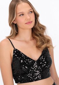 Fekete flitteres crop top vékony vállpántokkal, V-nyakú kialakítással, sima textúrával és fényes, tükröződő flitterekkel borított anyaggal.