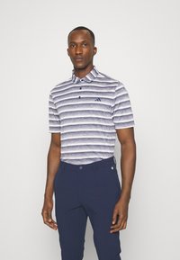 Polo tričko s golierom, s horizontálnymi modro-bielymi pruhmi, krátkymi rukávmi a malým výšivkovým logom. Vykombinované s námorníckymi nohavicami.