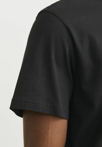 Sort bomulds T-shirt med korte ærmer, rund halsudskæring og diskret sømdetalje langs ærmekanterne.