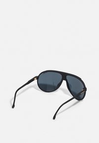 Sorte aviator solbriller med mørke linser, mat finish, slanke stenger og gull detaljer på rammen. Har et dristig, vinklet design.