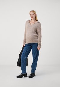 Pull à capuche en V beige clair, fabriqué à partir d'un matériau pelucheux. Associé à un jean droit bleu et des bottines à talons noires.