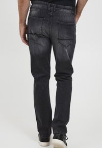 Jeans de mezclilla negra con un ligero desgaste, con corte recto, dos bolsillos traseros y una etiqueta de marca visible en la cinturilla.